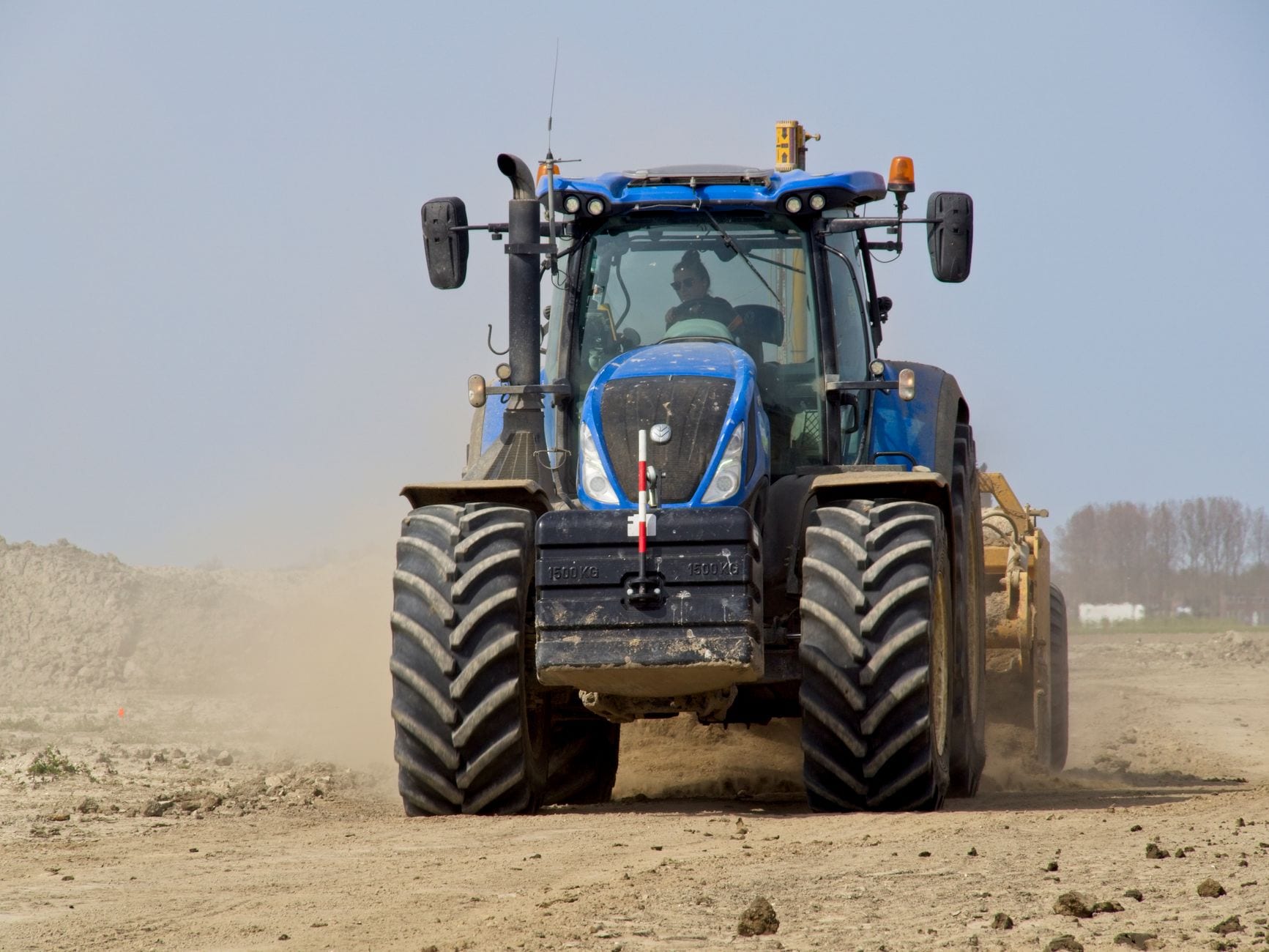 A powerful blue tractor operates on a dusty construction site in Noord-Holland, Netherlands.